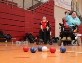 Mehrere Spieler*innen in der Halle, im Vordergrund des Bildes liegen blaue, weiße und rote Bälle
