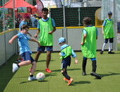 sechs Kinder und Jugendliche, vier davon in hellgrünen Leibchen, spielen Fußball auf einem von Banden begrenzten Spielfeld