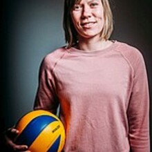 Katharina Pape steht mit Volleyball in der rechten Hand vor einem dunklen Hintergrund. 