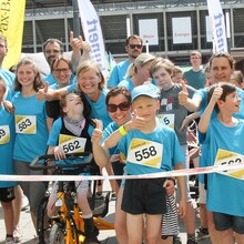 Eine fröhliche Gruppe von Erwachsenen und Kindern mit und ohne Behinderungen  in hellblauen T-Shirts hinter der Startlinie