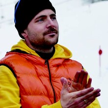 Martin Metz im Schnee mit Gelb-Orangener Jacke und Sonnenbrille auf schwarzer Mütze. Er applaudiert. 