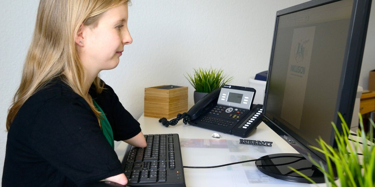Eine Frau mit verkürzten Armen bedient eine Tastatur am Computer.