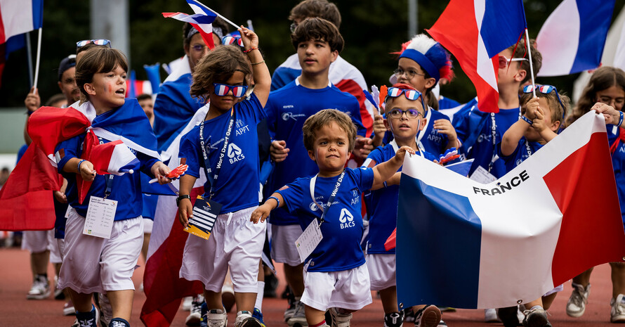 Die französische Nationalmannschaft beim Einlaufen mit Flaggen und Sonnenbrillen in ihren Landesfarben und dem ältesten Teilnehmer Odile mit 74 Jahren Mittendrin