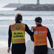 Ein Surfer und sein Coach machen sich am Strand auf dem Weg in Richtung Meer. 