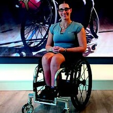 Katharina Krüger sitzt im Rollstuhl vor dem Plakat eines Rollstuhlbasketballspielers.