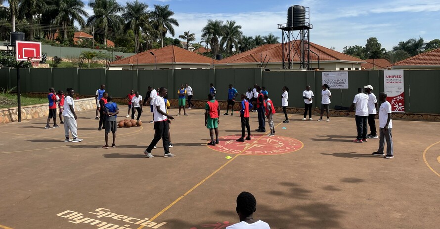 Ein Outdoor-Sportplatz mit Basketballkörben in Afrika und ca. 30 jungen Afrikaner*innen in unterschiedlichen Trikots